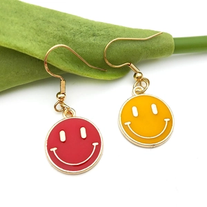 Close-up of red and yellow enamel smiley face earrings with golden hooks on green leaf
