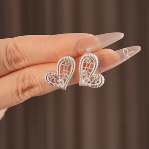 Detailed macro of silver heart earrings featuring hollow grid design and zircon stones