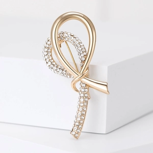 Detail of a gold ribbon brooch featuring sparkling rhinestones on a white pedestal