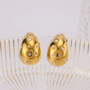 Detail of gold teardrop hollow earrings with inlaid rhinestones on a glass surface