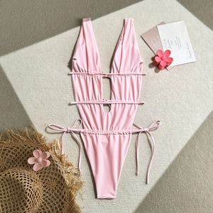 Flat lay of pink lace-up one-piece swimsuit with cutout details and summer accessories