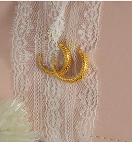 Detail of gold C-shaped earrings with unique dotted texture on pink leather background
