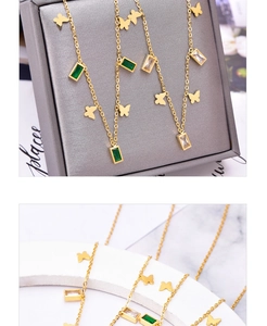 Close-up of gold butterfly pendant with green rectangular zircon on marble background