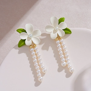 Detail of floral enamel earrings with pearls and gold tassel on cream display stand