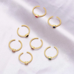 Close-up of golden beaded heart rings with colorful gems on purple satin background