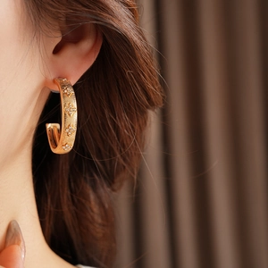 Close-up of gold C-shaped earring with diamond flower pattern worn by a model