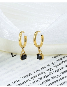 Detail view of gold hoop earrings with black zircon pendant on elegant silk background