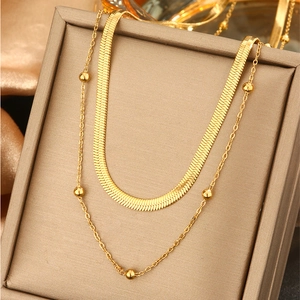 Detail of double-layer gold necklace featuring a flat snake chain and delicate bead chain