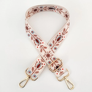 Detail of adjustable beige canvas strap with red and blue ethnic embroidery and gold hooks