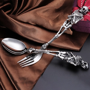 Detailed view of silver skull cutlery set featuring bone handles on brown silk fabric