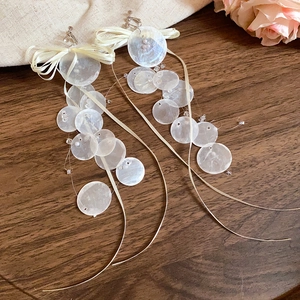 Detailed view of bamboo style shell earrings with white ribbon bows on wood background