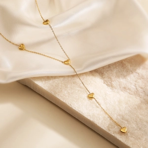 Golden Y-shaped necklace with five small heart pendants on silk and stone background