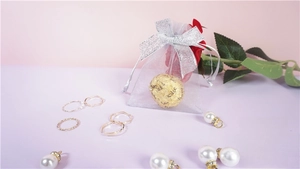 Macro shot of gold rings and pearl charms next to a white mesh drawstring gift bag