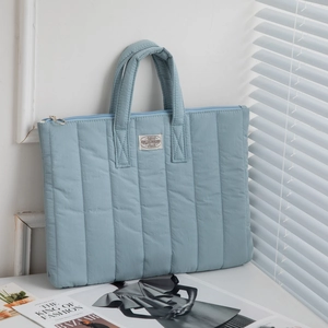 Close-up of quilted light blue laptop bag with top handles and brand label on desk