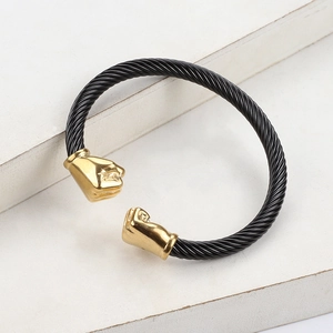 Silver stainless steel cable bracelet with gold fist ends on white podium