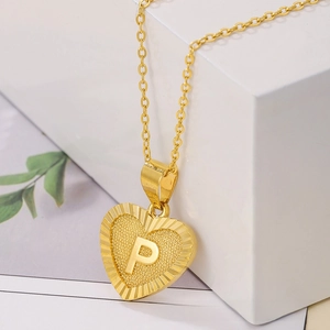 Detail of gold heart pendant necklace featuring embossed letter P and sunburst texture