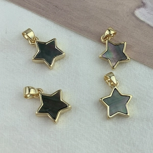 Vue macro de pendentifs étoile dorés avec incrustation de nacre noire sur tissu blanc