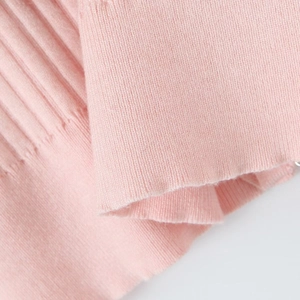 Gros plan du pull en tricot rose montrant la texture fine et les poignets côtelés