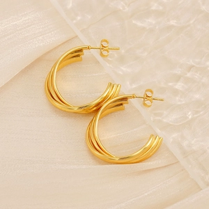 Macro detail of gold-plated triple layered C-shaped earrings on textured fabric