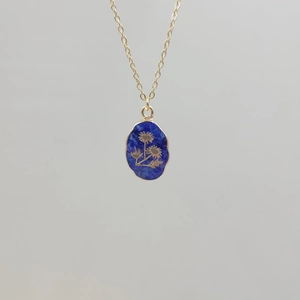 Detail of gold necklace with oval lapis lazuli pendant featuring engraved flower patterns