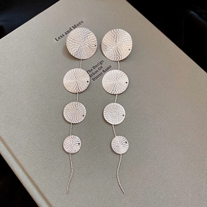 Detail of silver drop earrings with textured circular metal disks on a book background