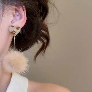 Detail shot of leopard print heart earrings with plush beige pompom on model