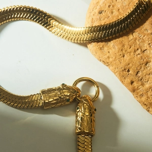 Golden flat snake bone necklace with green-eyed snake heads on a beige stone base