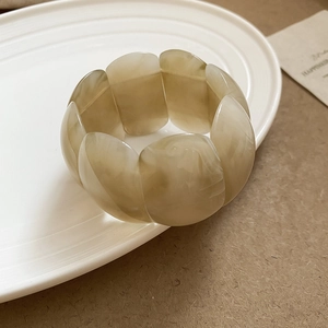 Detail of wide acrylic slice bracelet with cream marble texture and elastic connection