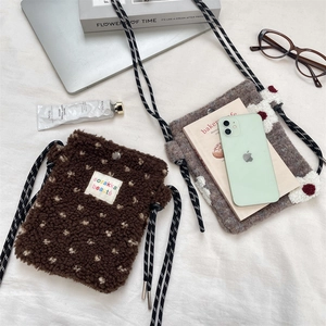 Detail of plush lamb-like crossbody phone bags with woven straps and button closure