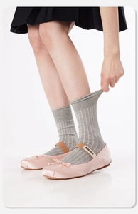 Nahaufnahme der rosa Satin-Ballerinas mit grauen gerippten Socken und Schleife