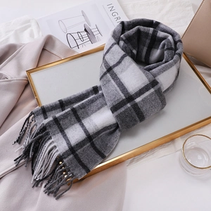 Detailed view of grey plaid wool scarf with fringe on a golden decorative tray