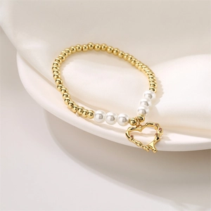 Detalle de una pulsera de cuentas doradas con perlas blancas y colgante de corazón en plato blanco