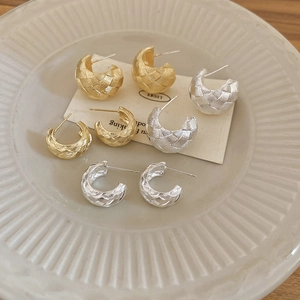 Detailed view of C-shaped woven texture earrings in gold and silver finish on a tray
