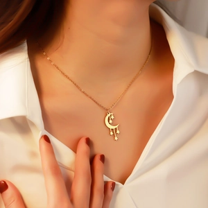 Close-up of golden star and moon pendant necklace worn by model on white shirt