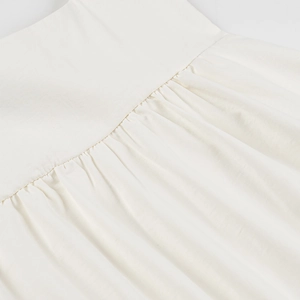 Detailed close-up of white fabric texture with ruched pleated waist and fine stitching