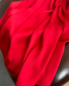 Detailed view of red silk satin scarf texture with elegant folds on a leather surface