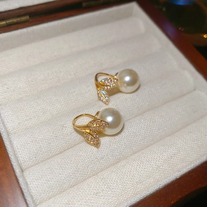 Detail of elegant gold fishtail leaf earrings with white pearls in a velvet jewelry box
