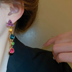 Close-up of gold dangle earring with multi-colored gemstones worn by a model