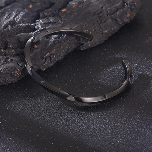 Macro detail of black Mobius twist stainless steel cuff bracelet on dark textured stone