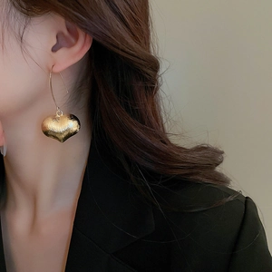 Detail of vintage heart drop earrings with hammered gold texture on a female model