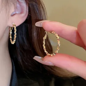 Textured gold geometric hoop earrings with reflective square pattern worn by a model