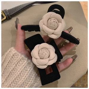 Macro detail of black velvet hair claws with elegant creamy white camellia flower decoration