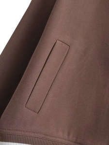 Detail of brown jacket side pocket with white striped ribbed hem and smooth fabric texture