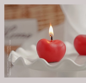 Primer plano de una vela aromática en forma de manzana roja sobre base ondulada