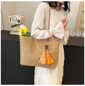 Close-up of woven straw tote bag featuring decorative orange and yellow tassels accessory