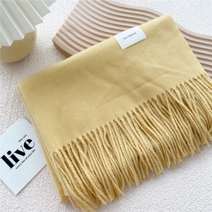 Detail of warm yellow scarf with fringe on wooden tray against white wall