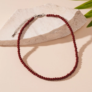 Dettaglio collana con perline di cristallo rosso e chiusura argento su marmo bianco