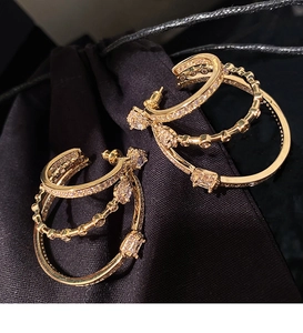 Detail of gold layered hoop earrings with zircon stones on a dark textured background