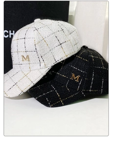 Detail of tweed baseball caps showing metallic M logo and woven fabric texture