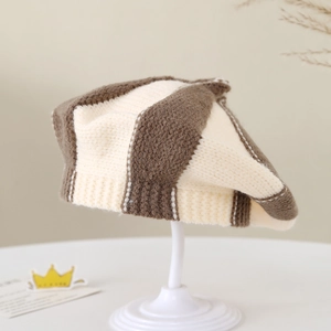 Close-up of baby striped knit beret in brown and beige with ribbed edge and top knot